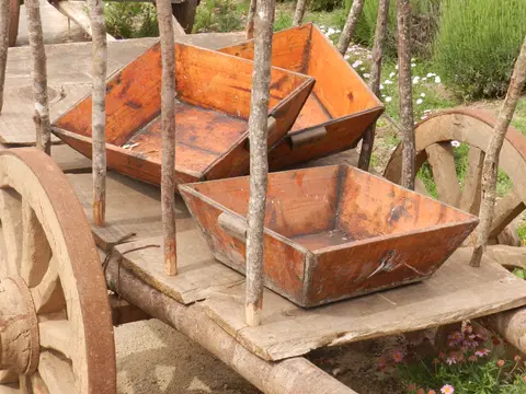 Antique wooden harvest trays painted orange, resting on an old ox cart beside lavender