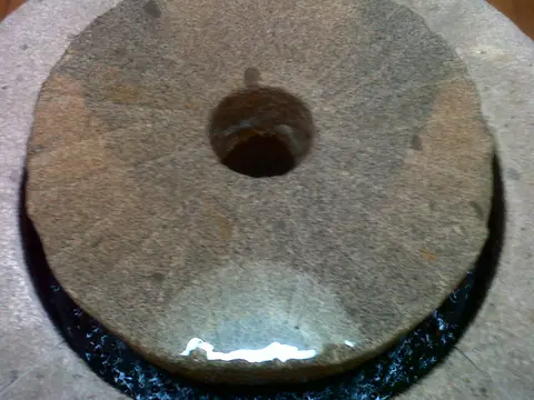 Old circular stone grinding wheel with a worn central hole, resting flat on a wooden floor