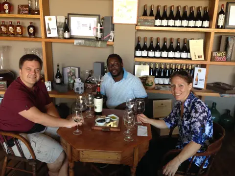 Three guests seated at a tasting table with wine and a cheese board in the Bodegas RE shop, shelves of RE bottles behind