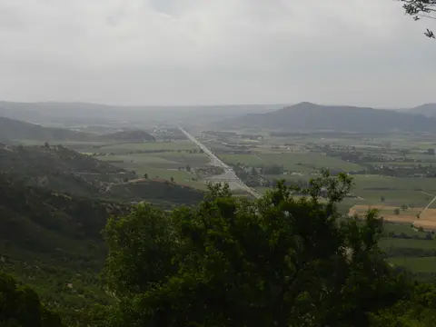 Wide view across a green valley of vineyards and fields from a hillside, with the highway running through it