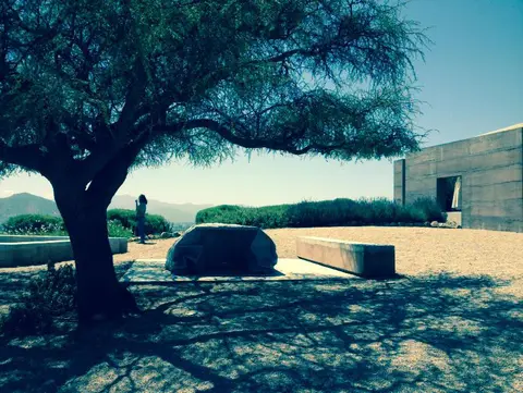 Concrete winery building and gravel courtyard under a broad shade tree, mountains behind