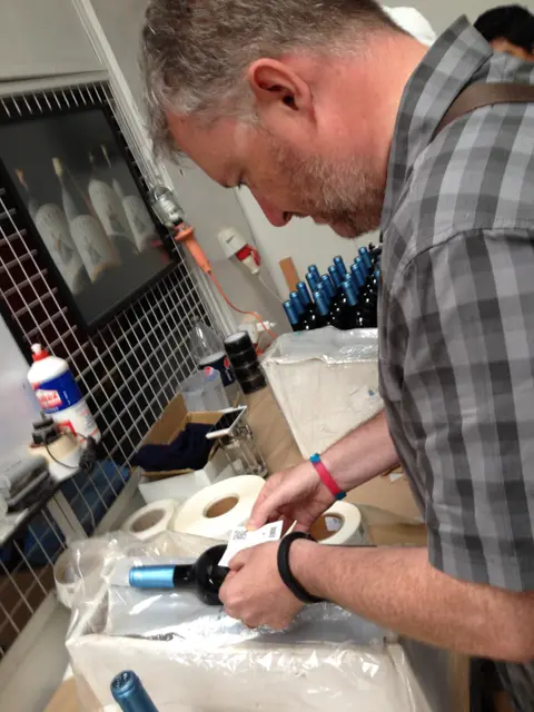 Close view of hands smoothing a label onto a wine bottle at a labelling bench