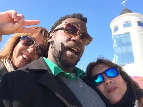 Guide and two guests taking a selfie in front of a white tower building on a clear day