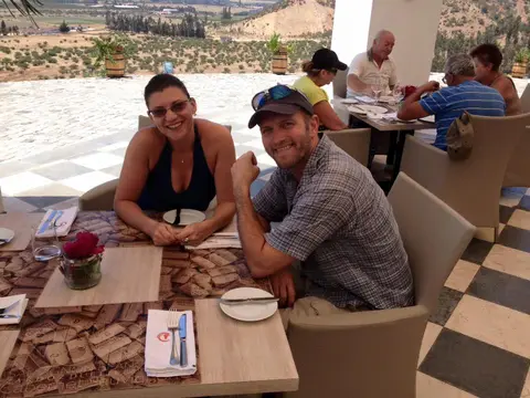 Couple at a restaurant table on a terrace overlooking olive groves and hills