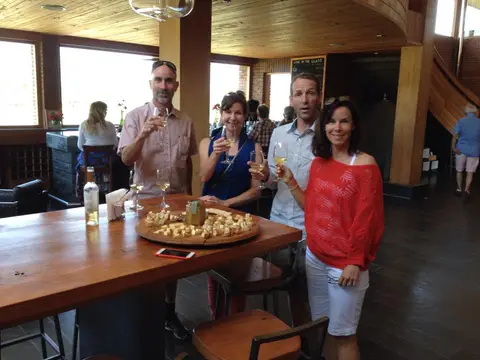 Four guests raising glasses of white wine in a modern winery tasting room with a cheese board