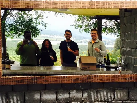 Four guests with wine glasses at an open-air stone tasting bar looking out over vineyards