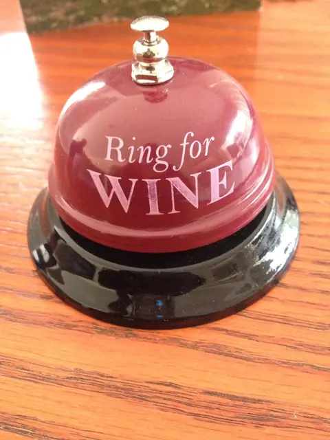 Red desk bell reading "Ring for Wine" on a polished wooden tasting table
