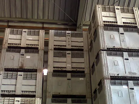 Tall stacks of grey plastic harvest bins under a metal winery roof, one marked VTN 132