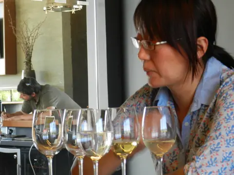 Line of white wine glasses along a tasting bar with a host beside them