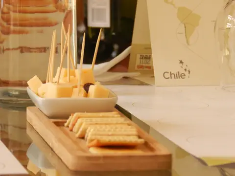 Cheese cubes and crackers served on a wooden board beside a wine bottle and glasses