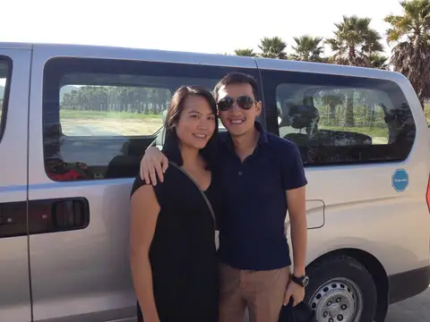 Couple standing beside the tour van at a vineyard, palms and vine rows behind