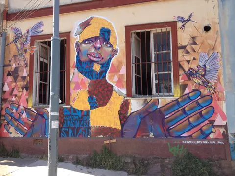 Large mural of a figure with outstretched hands and hummingbirds, painted across a house front on Cerro Alegre, Valparaíso