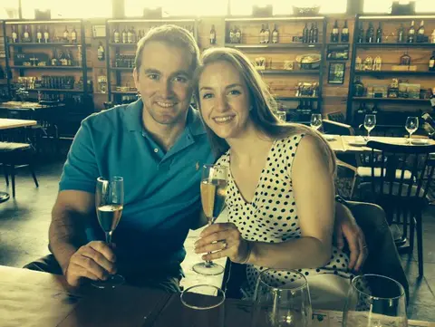 Couple toasting with sparkling wine at a winery bar lined with shelves of bottles