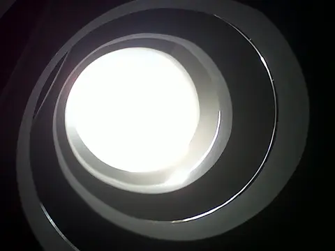 Looking straight up through concentric circular openings to a bright round skylight above a cellar