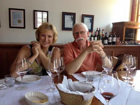 Couple seated at a laid table in a winery dining room, awards framed on the wall behind