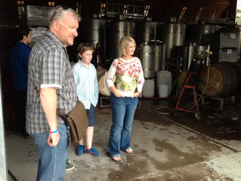 Family group standing between fermentation tanks and oak barrels in a winery cellar