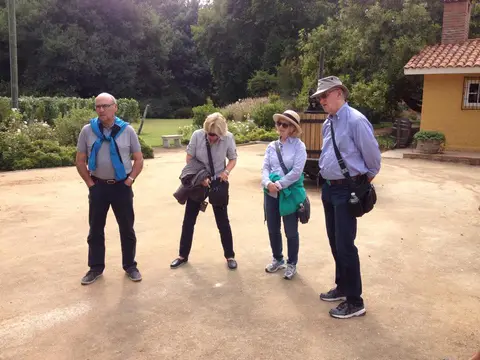 Four guests standing beside an antique wooden wine press in a winery garden