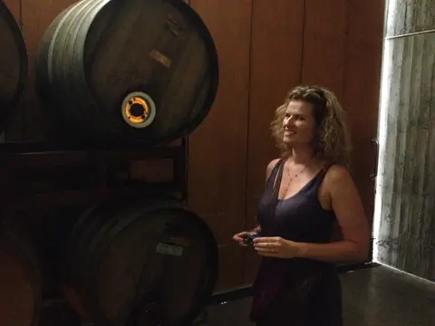 Winery host standing beside two large dark oak casks, one lit through the bung hole