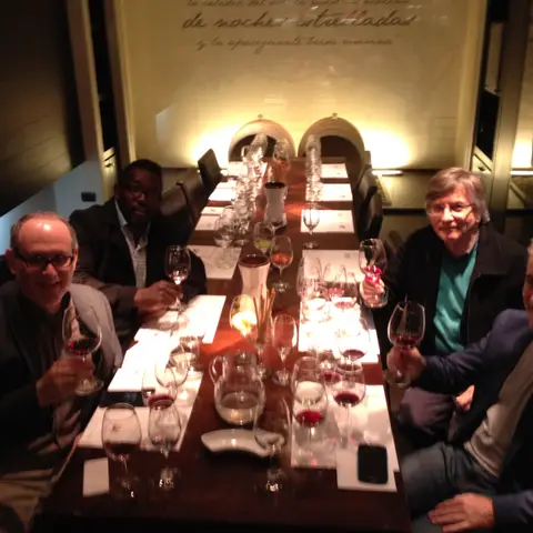 Group raising glasses along a long table in a warmly lit winery dining room, a Spanish inscription painted on the far wall