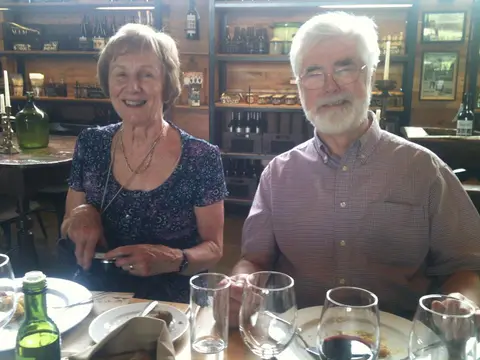 Older couple seated at a tasting table in a winery shop lined with bottles and glassware
