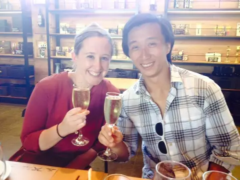 Couple toasting with sparkling wine in a winery shop lined with shelves of bottles