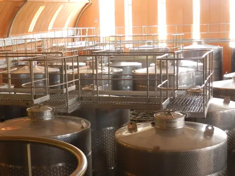 Rows of stainless steel fermentation tanks with walkways beneath a curved wooden ceiling