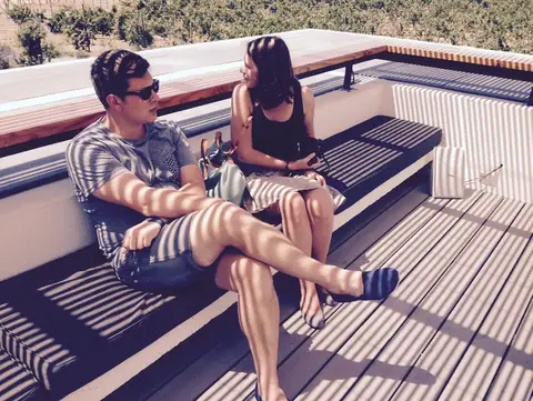Couple sitting and talking on a sunny winery terrace with vines behind