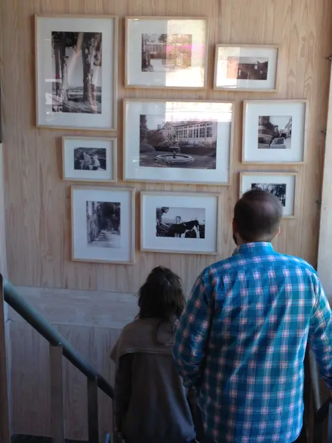 Two visitors looking at a wall of framed black-and-white family photographs in a pale wood winery stairwell